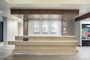 Una recepción con un cartel de 'Hilton', un muro con diseño y una máquina expendedora al fondo.