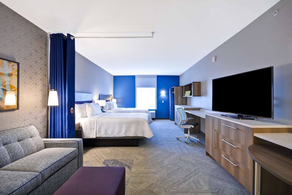 A hotel room with a bed, a sofa, a desk, a TV, and a window.