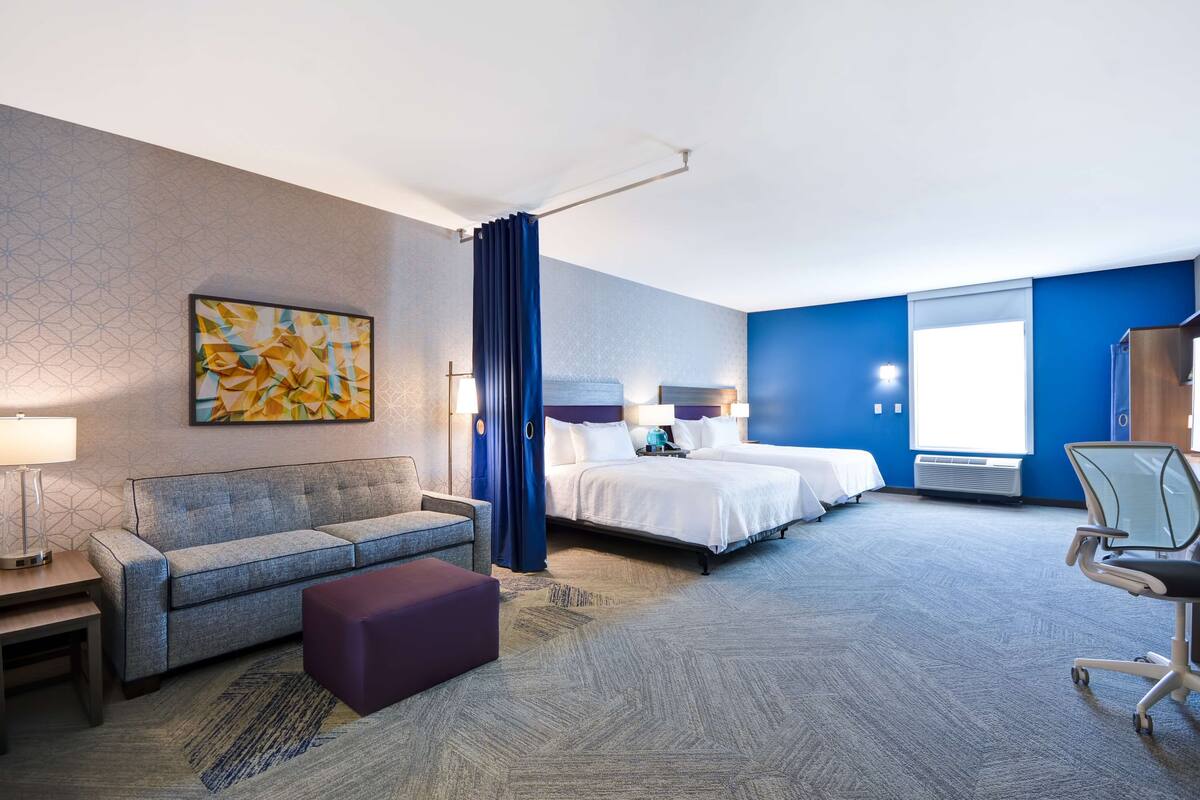 A hotel room with a sofa, a bed, a desk, a chair, and a large window.