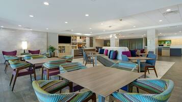 A spacious hotel lobby with multiple seating areas, including a central sofa and several tables with chairs.