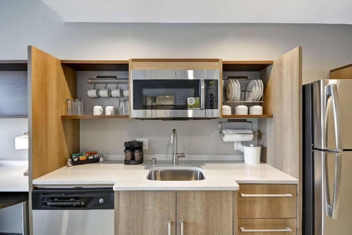A modern kitchen with a built-in microwave, stainless steel refrigerator, and wooden cabinets.