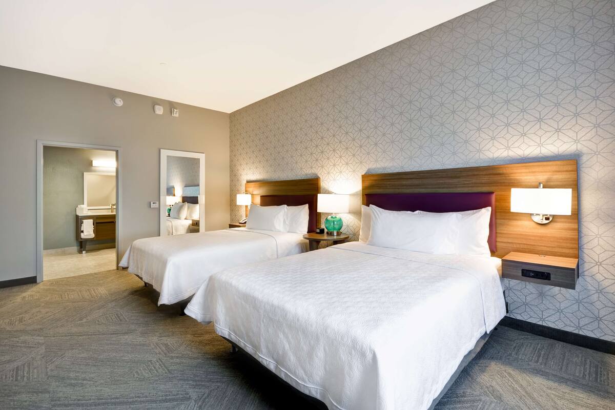 A hotel room with two beds, a bathroom, and a geometric patterned wall.