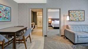 Habitación de hotel con comedor, sofá, cama y baño visible a través de una puerta abierta.