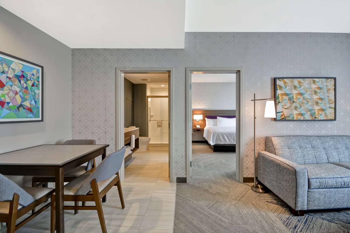 A hotel room with a dining area, a sofa, a bed, and a bathroom visible through an open door.