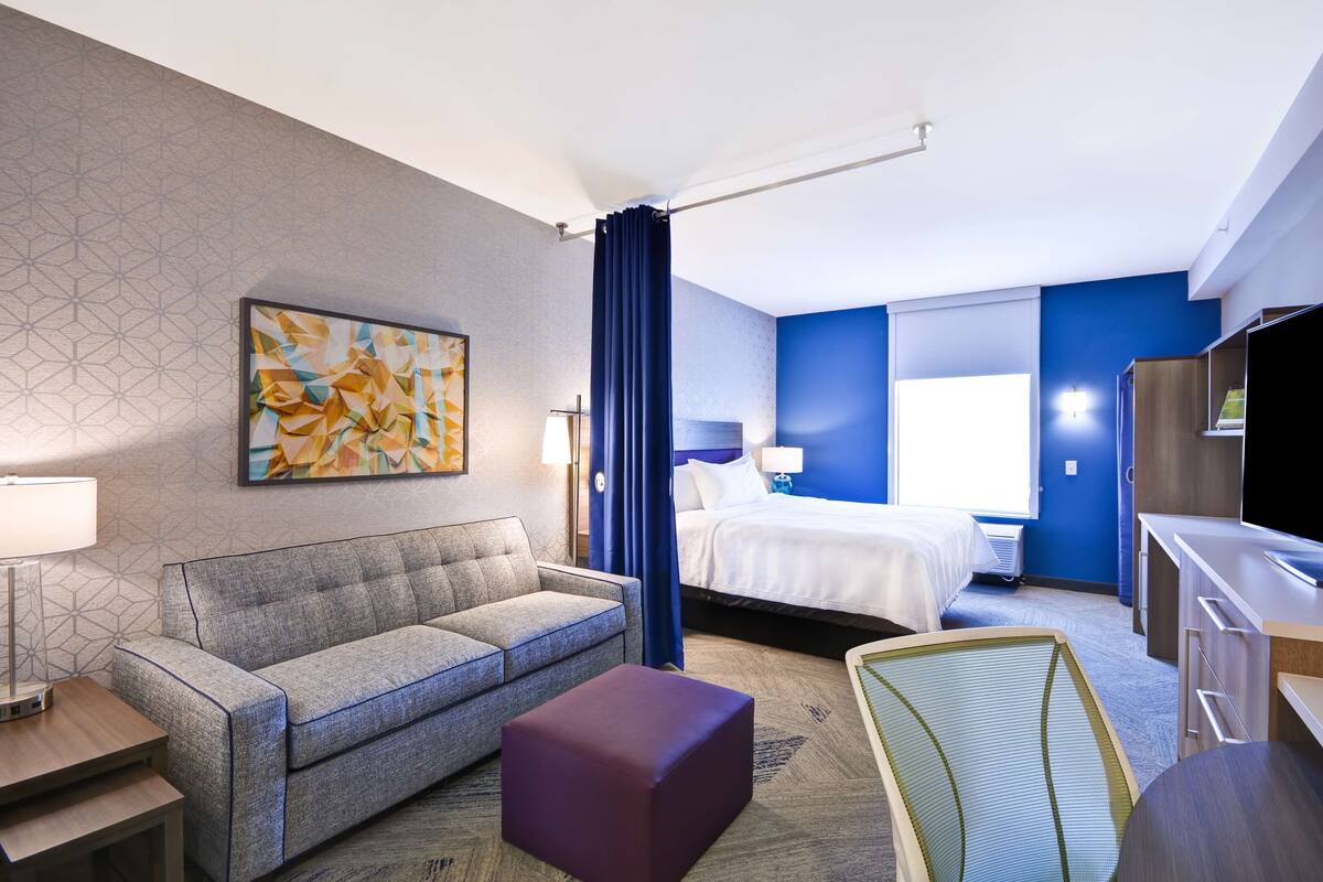 A hotel room with a sofa, a bed, a desk, and a television.