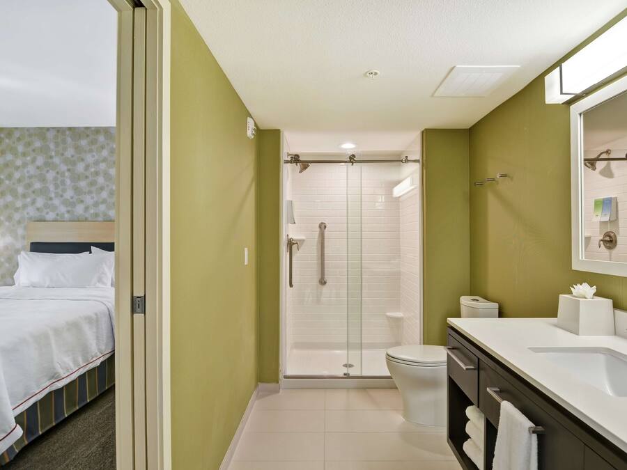Une salle de bain d’hôtel équipée d’une douche, de toilettes et d’un lavabo, et une chambre adjacente avec un lit.
