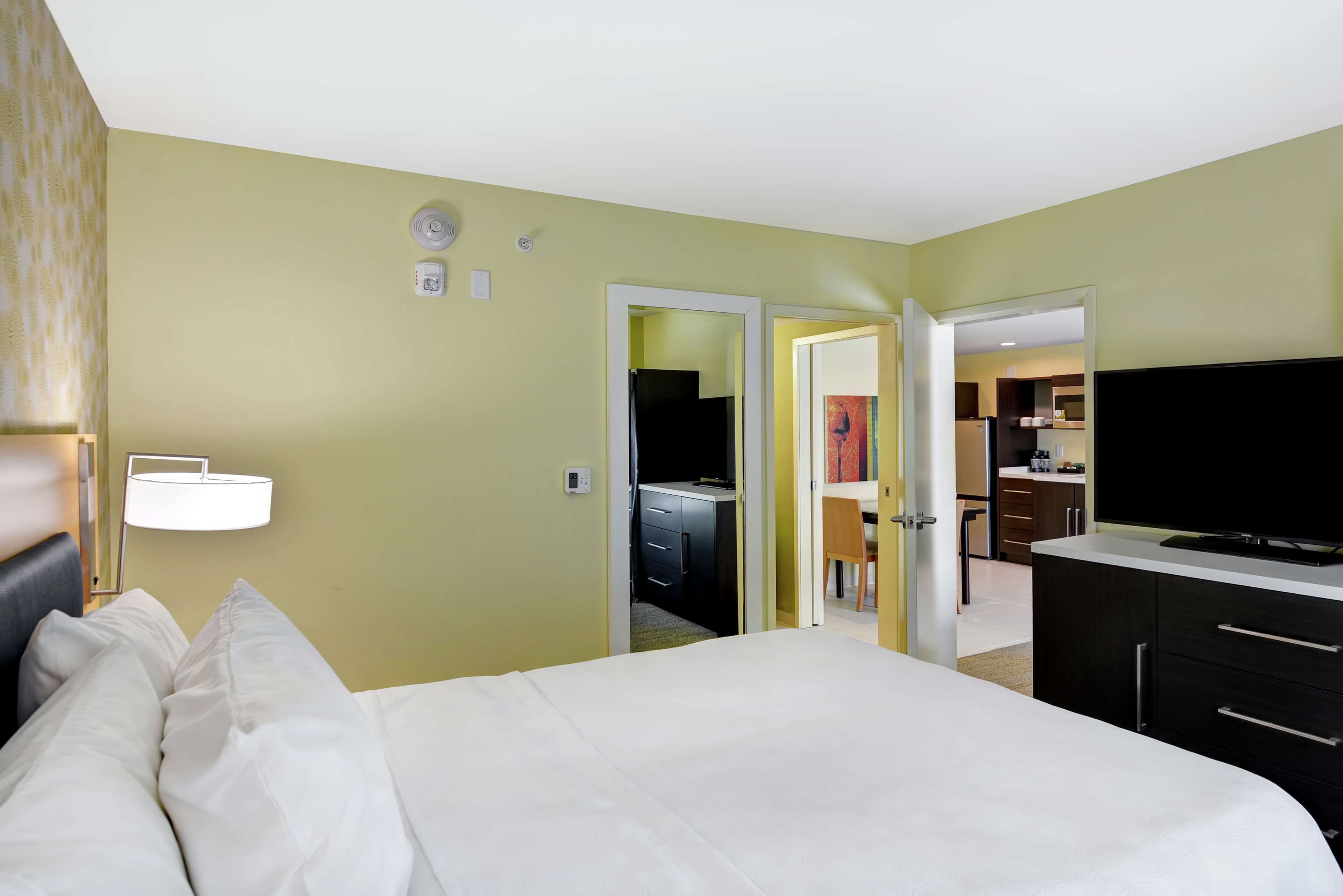 A hotel room with a bed, a TV, a desk, and a kitchenette.