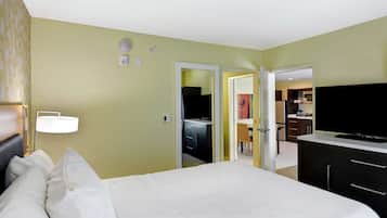 A hotel room with a bed, a TV, a desk, and a kitchenette.