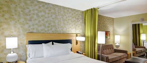 A hotel room with a bed, two bedside tables with lamps, a chair, a sofa, and a mirror.