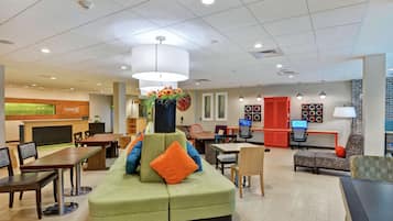 A spacious lobby with a green sofa, wooden tables, and a reception desk.