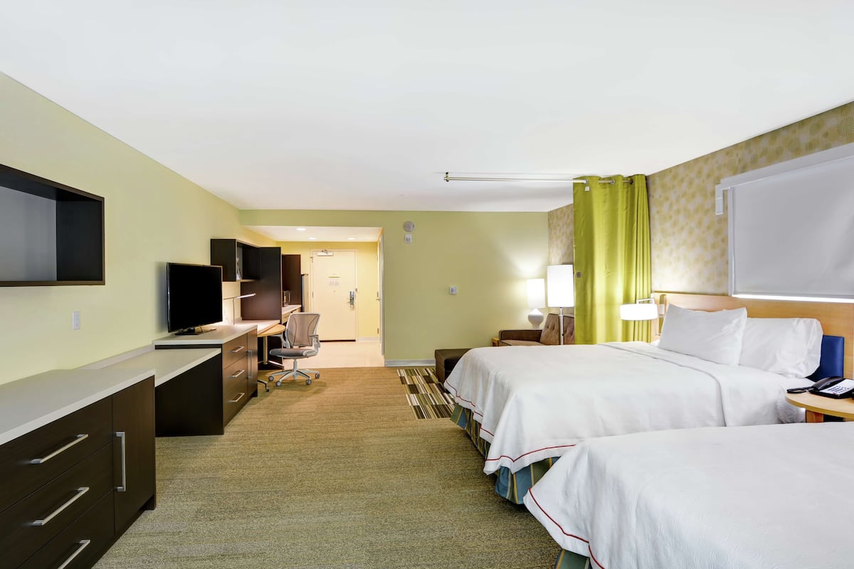 A hotel room with two beds, a desk, a television, and a bathroom visible in the background.