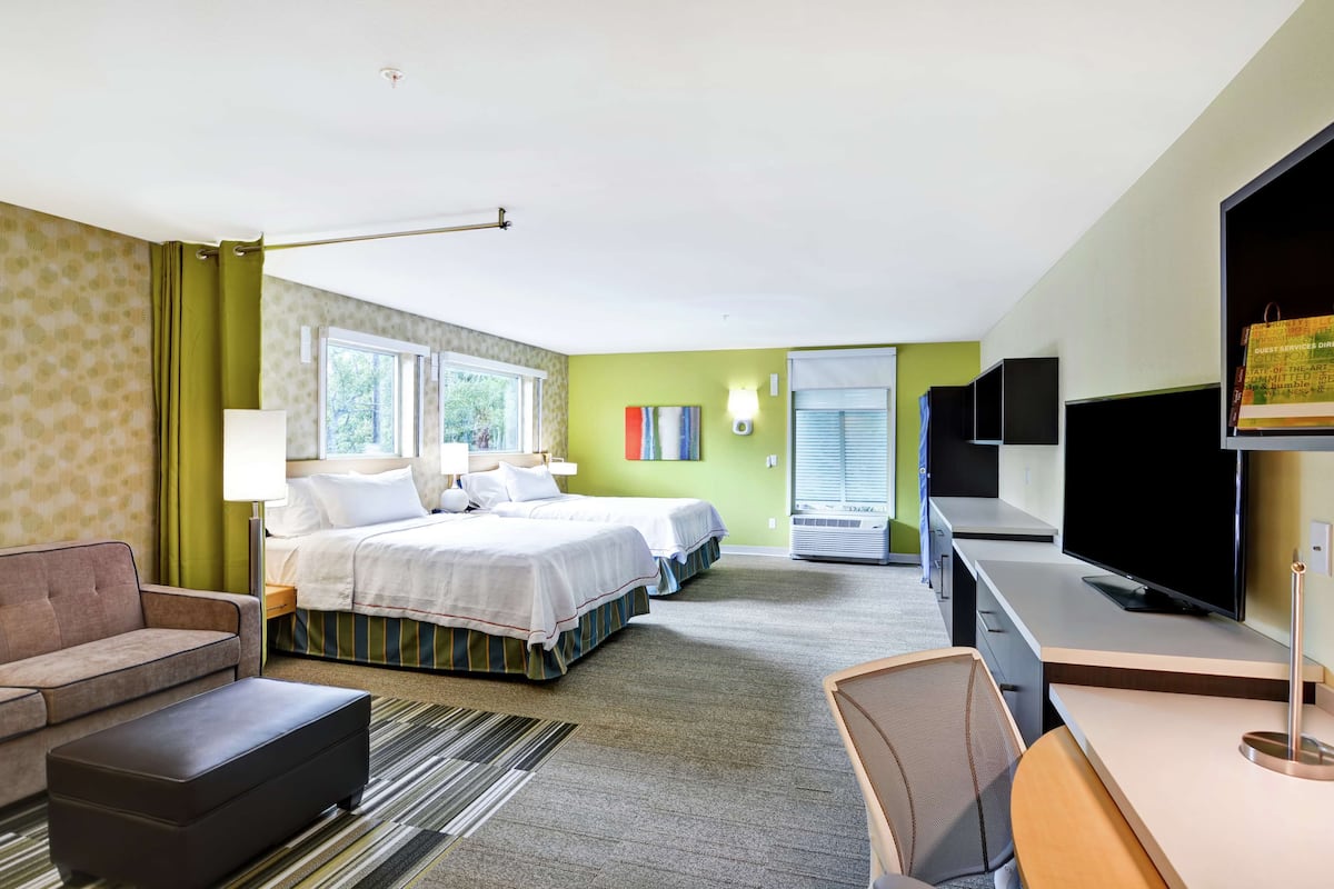 A hotel room with two beds, a desk, a TV, and a sofa.