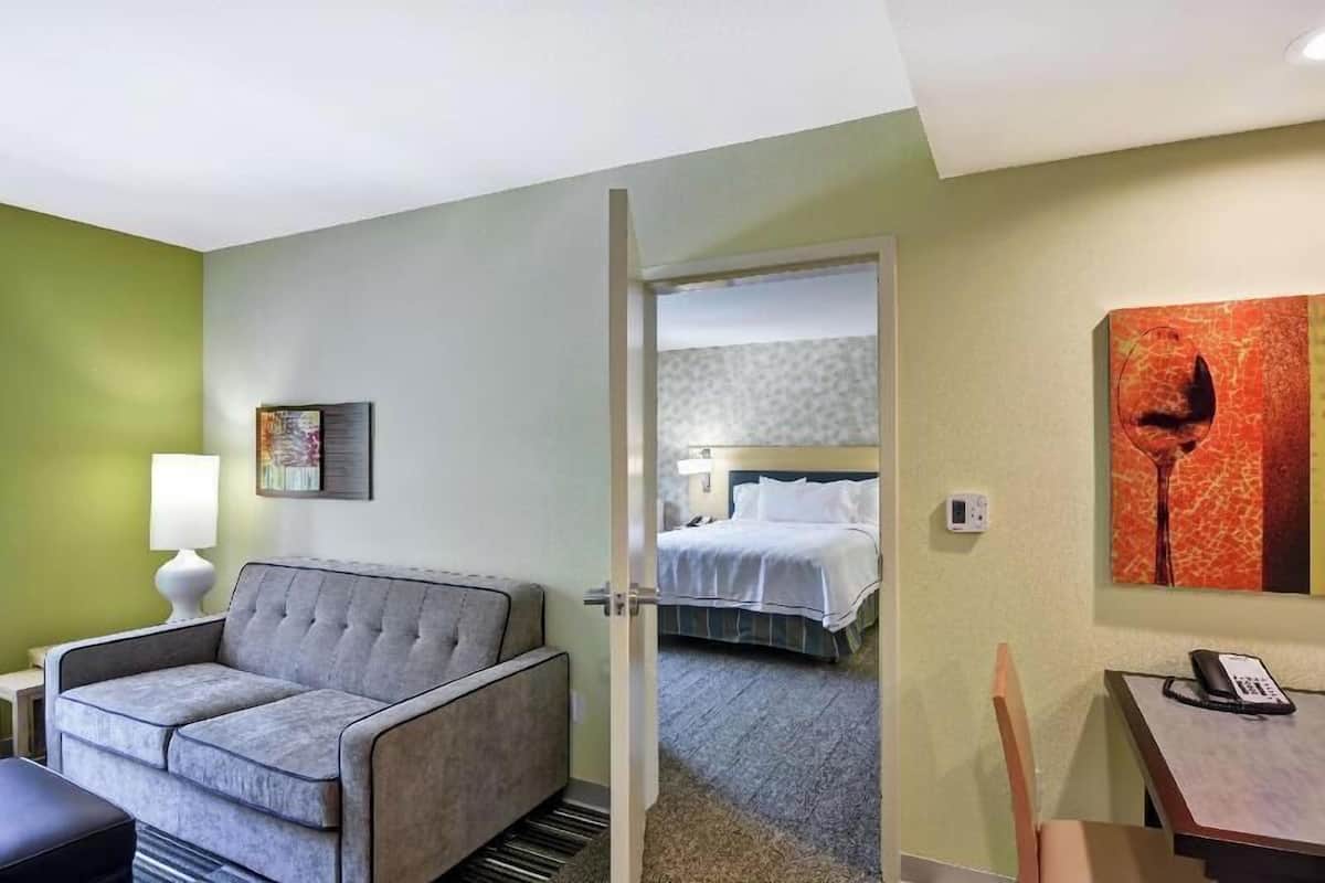 A hotel room with a grey sofa, a bed, a painting, and a telephone on a table.