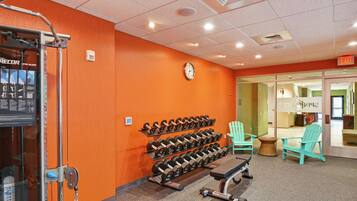 A gym with orange walls, a clock, and rows of dumbbells.