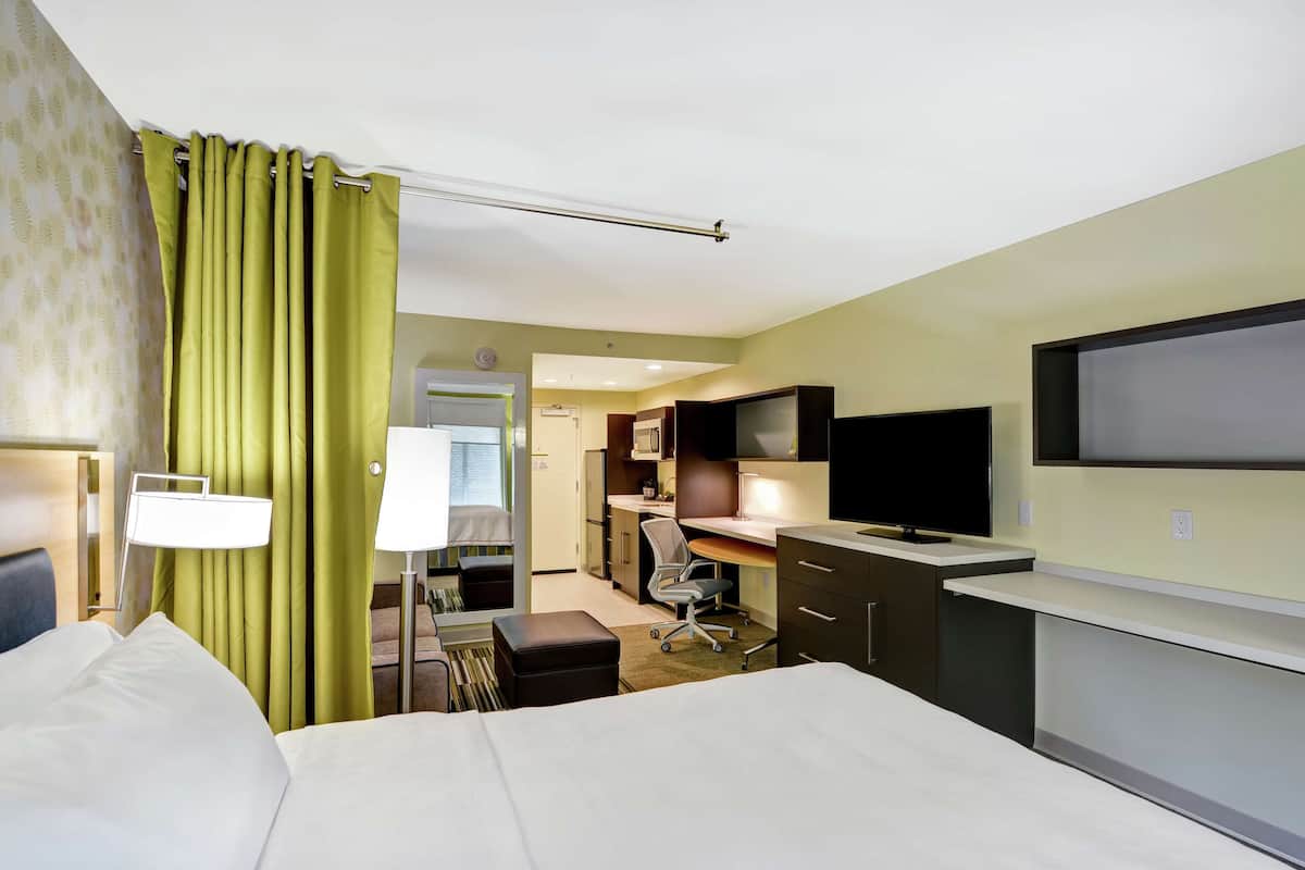 A hotel room with a bed, a desk, a chair, a television, and a bathroom visible through an open door.