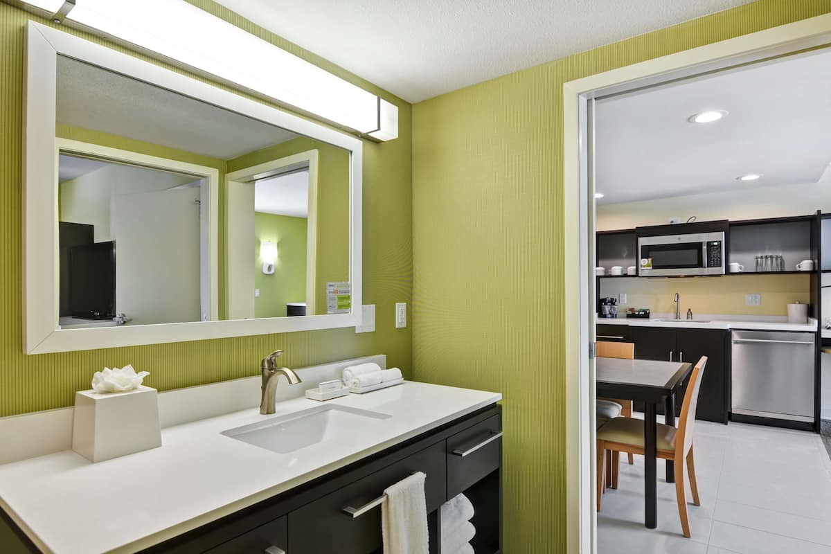 A modern bathroom with a white sink, a large mirror, and a green wall.