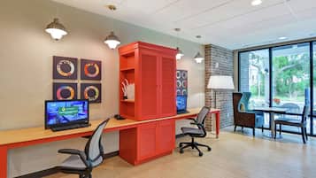 Un espace de bureau moderne comprenant deux bureaux, des chaises, un meuble rouge et des œuvres d’art accrochées aux murs.