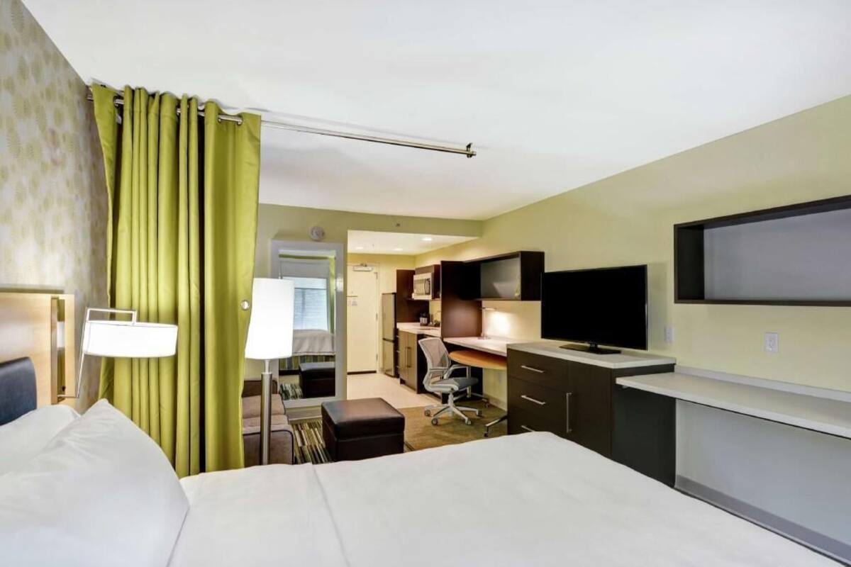 A hotel room with a bed, desk, chair, television, and a bathroom visible through an open door.