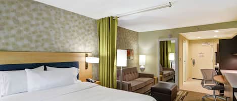 Una habitación de hotel con una cama grande, un escritorio, una silla, un sofá y un espejo.