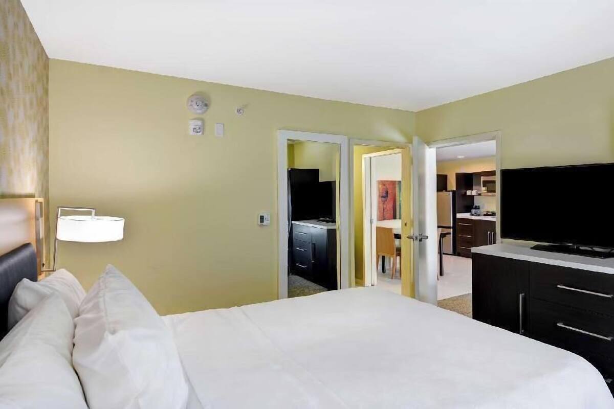 Una habitación de hotel con cama, televisión, escritorio y kitchenette.