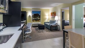 A modern hotel room with a kitchenette, a sofa, a dining table, and a view of the cityscape. - Home2 Suites by Hilton Kansas City Downtown (Kansas City)