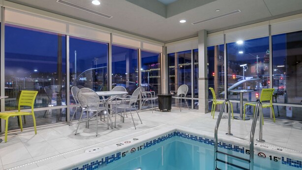 A pool area with a view of the city at night, including a pool with a blue tiled edge, a ladder, and several chairs and tables. - Home2 Suites by Hilton Kansas City Downtown (Kansas City)