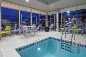 A pool area with a view of the city at night, including a pool with a blue tiled edge, a ladder, and several chairs and tables. - Home2 Suites by Hilton Kansas City Downtown (Kansas City)