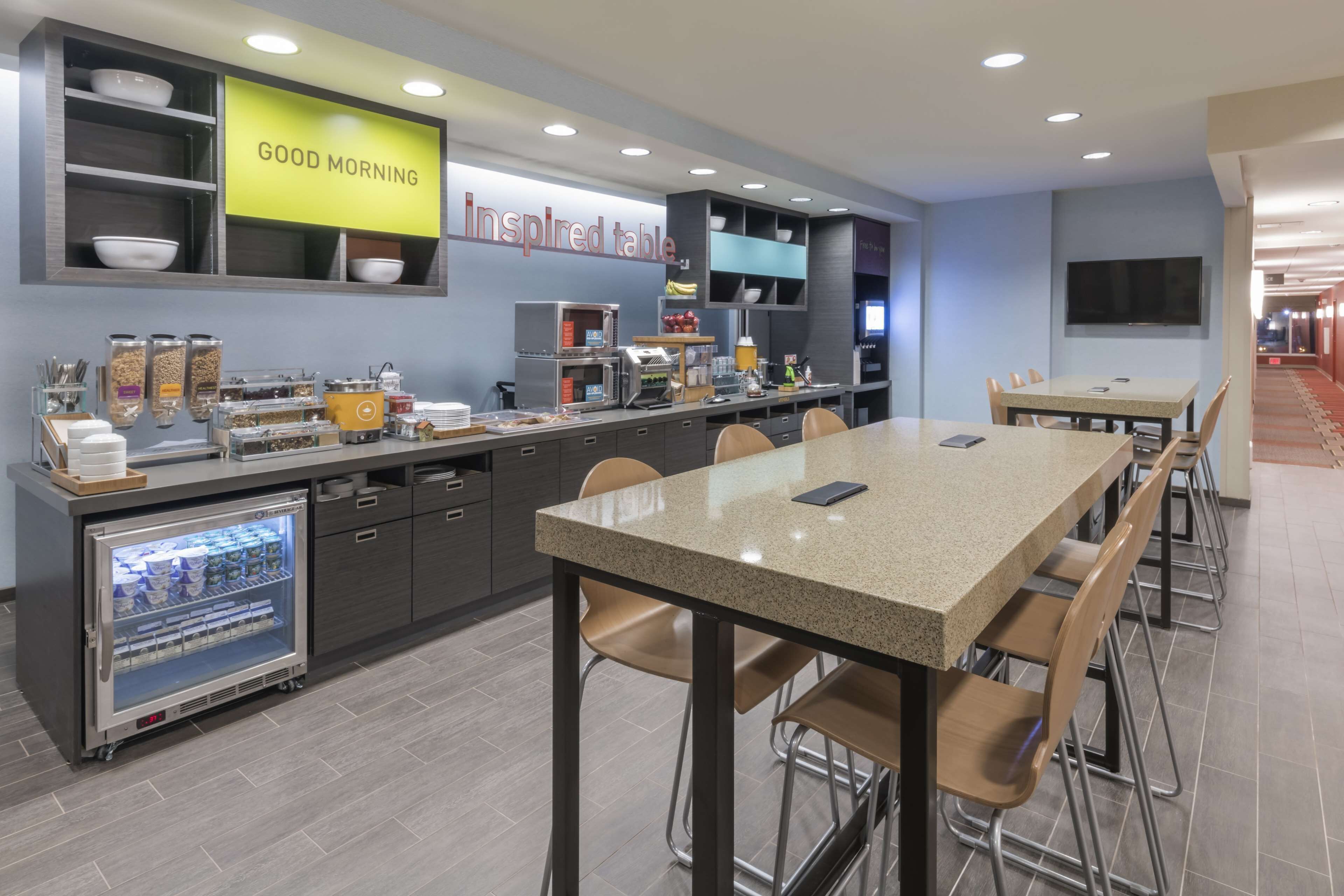 A modern breakfast area with a self-service station, a refrigerator, and a dining table with chairs.