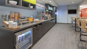 A modern breakfast bar with a variety of food options, a refrigerator with beverages, and a seating area with chairs. - Home2 Suites by Hilton Kansas City Downtown (Kansas City)