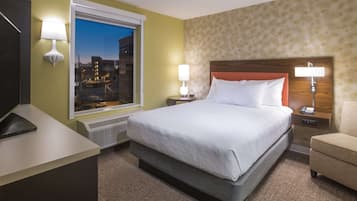 A hotel room with a large bed, two bedside tables, a desk, and a window with a city view.