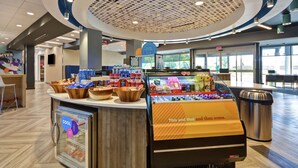 A food display area with a variety of snacks and beverages, a glass case labeled "COOL", and a sign that reads "This and that and then some." - Tru by Hilton Sumter (Sumter)