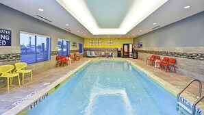 An indoor swimming pool with clear water, surrounded by yellow and red chairs, and a tiled wall with a 'Watering' sign. - Tru by Hilton Sumter (Sumter)