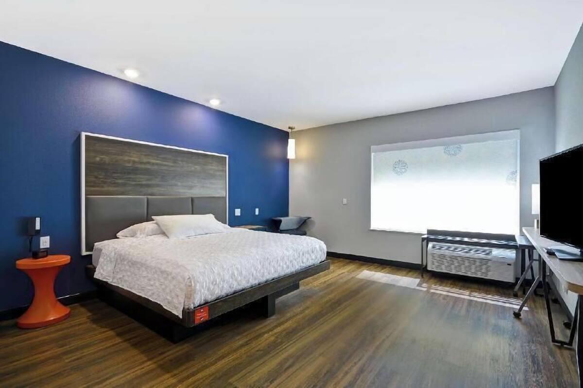 A modern hotel room with a bed, a TV, a window with a view, and a small table.