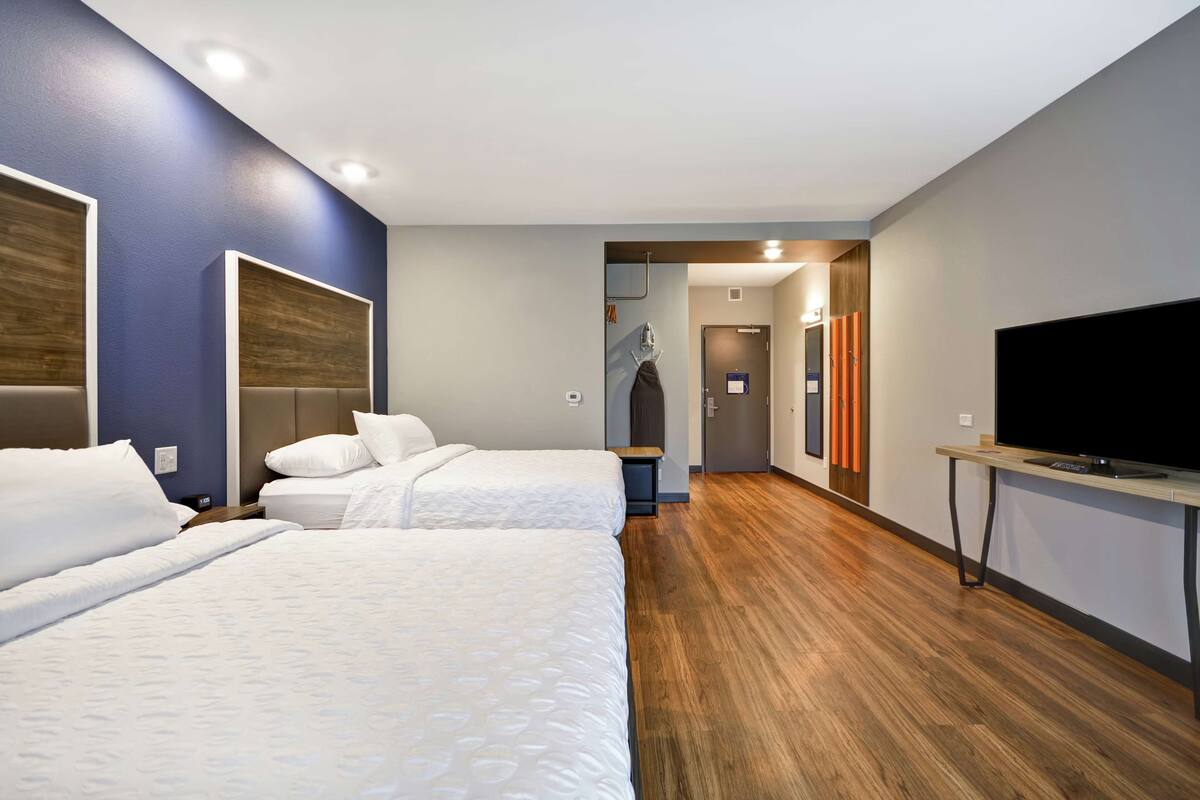 A hotel room with two beds, a TV, and a wooden floor.
