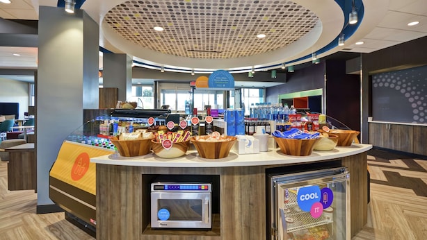 A self-service breakfast area with a coffee machine, refrigerated display, and various food items. - Tru by Hilton Sumter (Sumter)