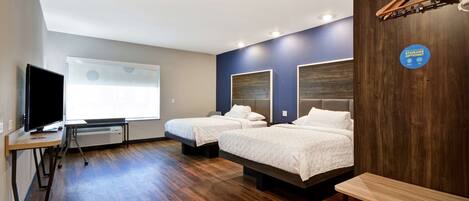A hotel room with two beds, a desk, a television, and a large window.