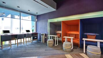 A modern office space with a long desk area, multiple chairs, and a seating area with ottomans and tables.
