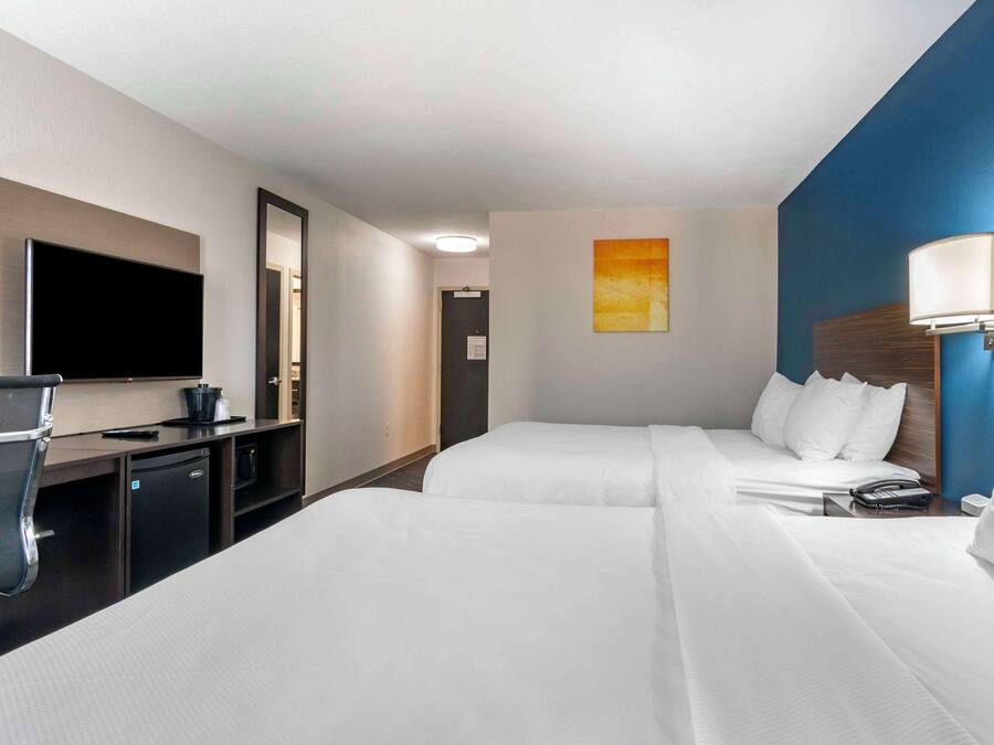 A hotel room with two beds, a desk with a flat-screen TV, a mirror, a painting, and a nightstand with a lamp.