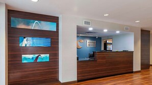 A hotel reception area with a wooden reception desk, a blue wall with a MainStay Suites sign, and artwork depicting bridges. - Comfort Inn St. Louis Airport (Bridgeton)