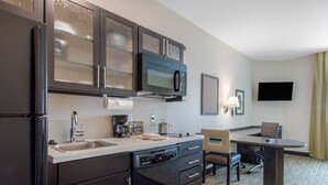 A compact kitchen with a refrigerator, microwave, and dishwasher, a small sink, and a dining area with a chair and table. - Candlewood Suites San Antonio Lackland AFB Area by IHG (San Antonio)