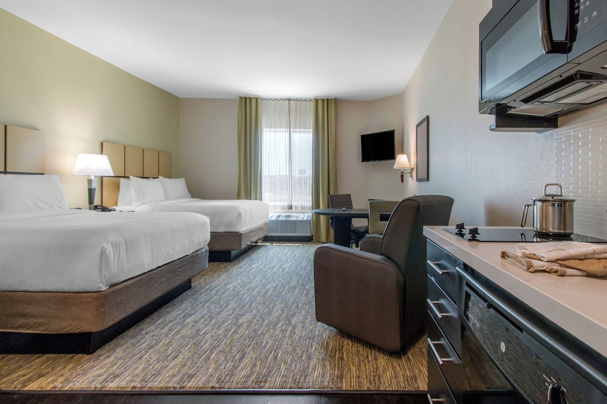A hotel room with two beds, a desk, a chair, a television, and a kitchenette.