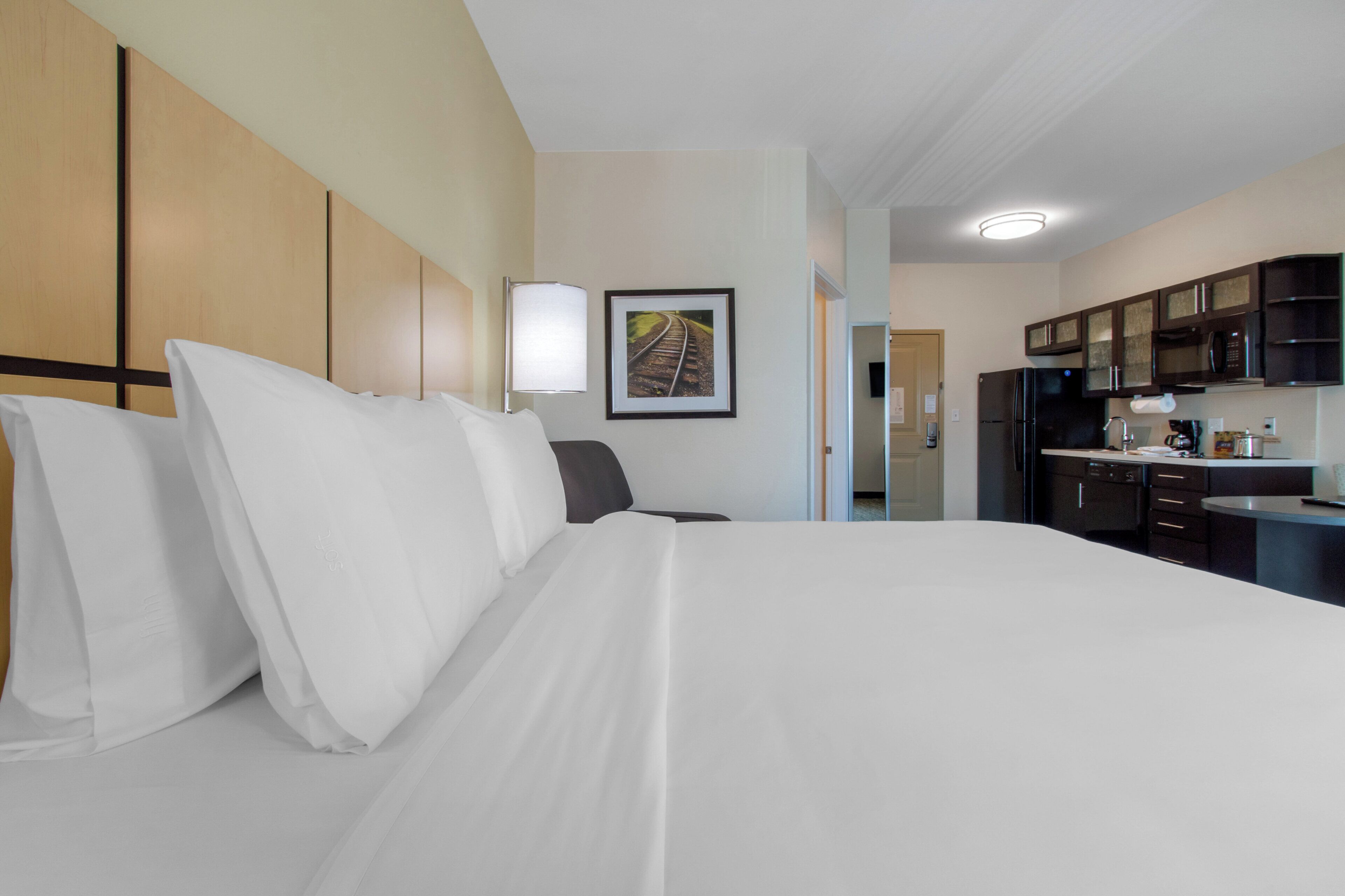Ett hotellrum med en stor säng, ett skrivbord och ett litet kök.