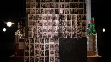 A wall with a collage of black and white photos, a bottle of liquor, and a wrapped bottle of soda.
