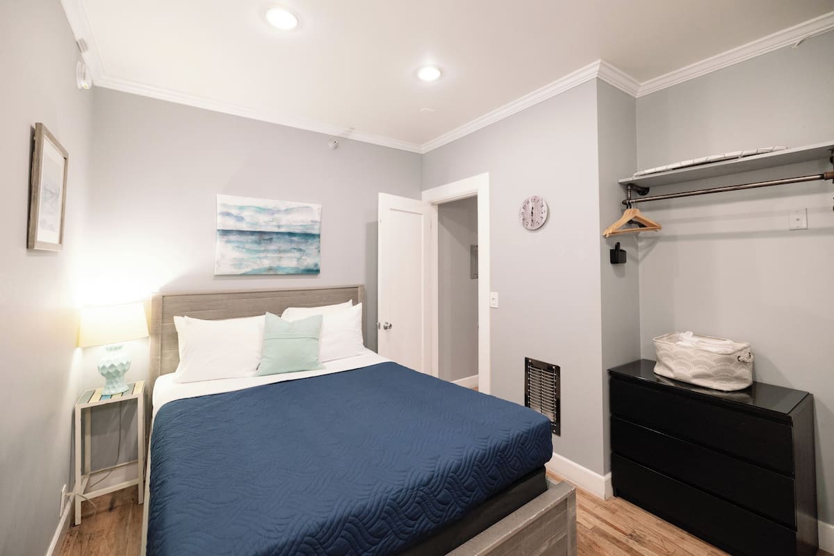 Une chambre à coucher comprenant un lit, une table de chevet, une commode, une horloge murale et un tableau.