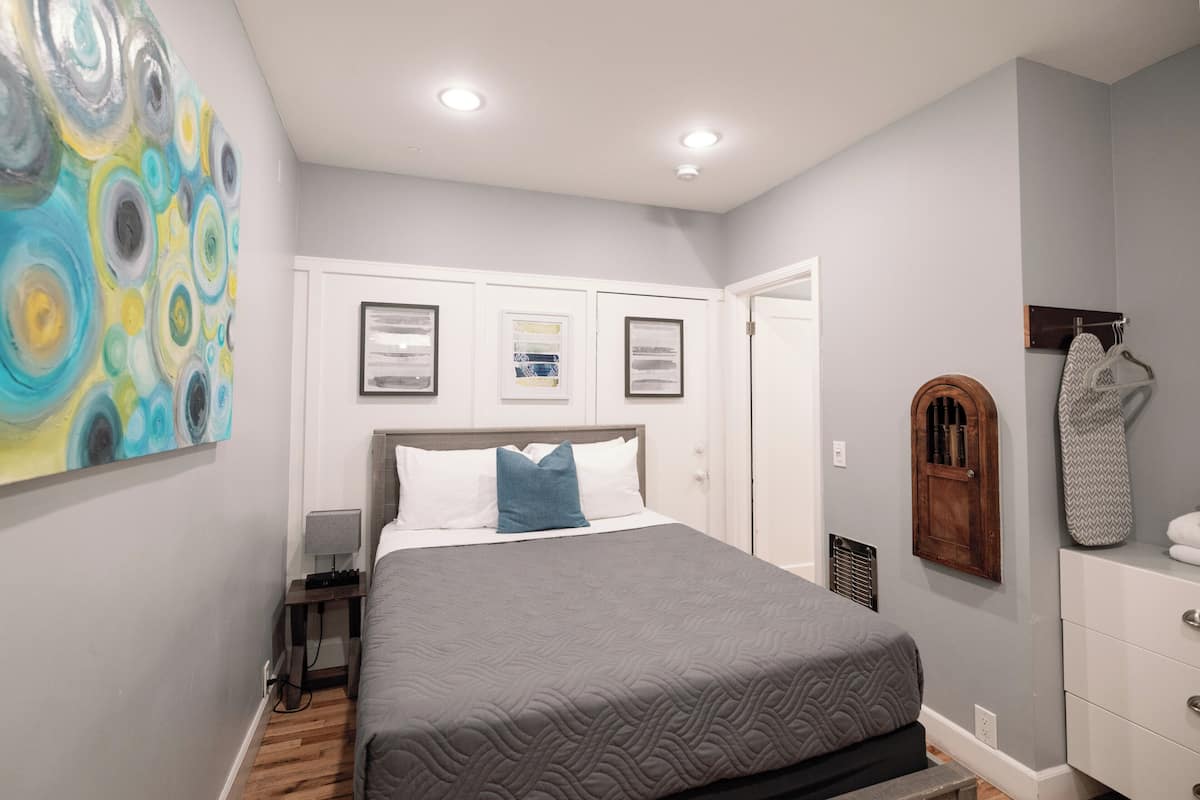 Une chambre à coucher comprenant un lit, une table de chevet, une commode et une planche à repasser fixée au mur.