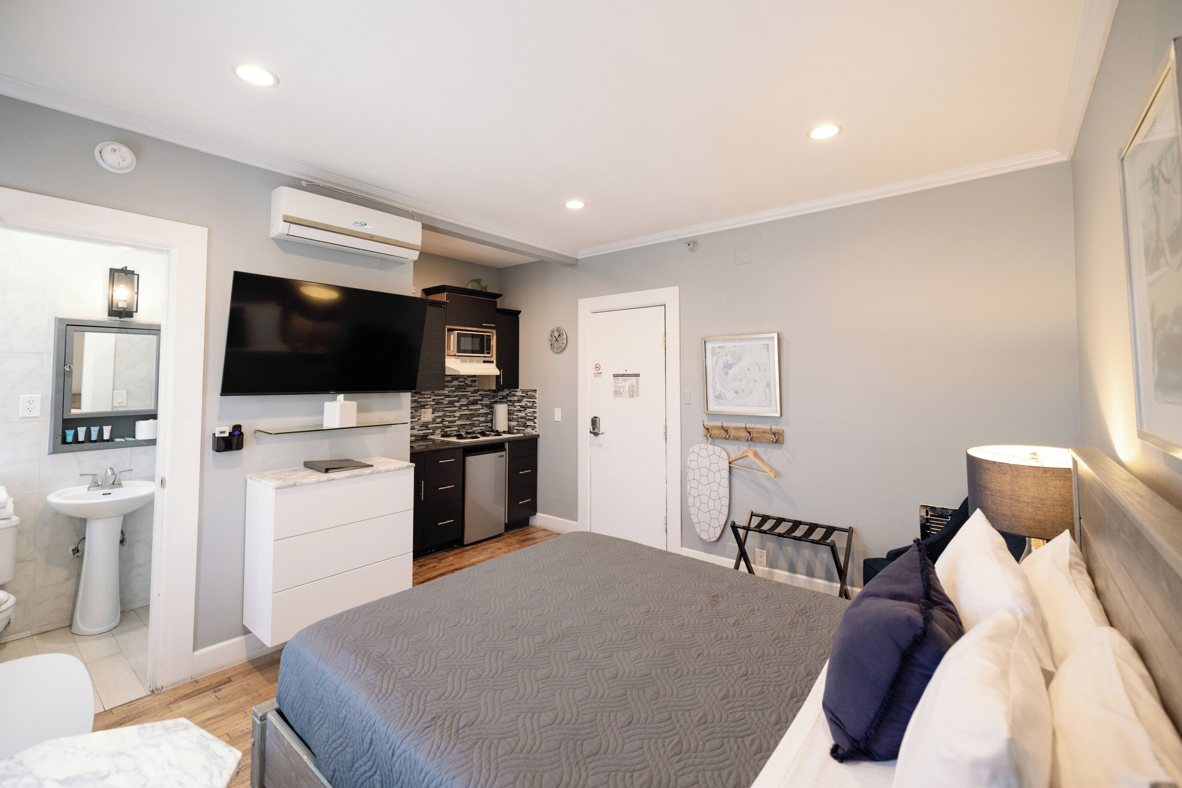 A modern hotel room with a large bed, a flat-screen TV, a kitchenette, and a bathroom.