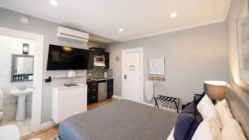 A modern hotel room with a large bed, a flat-screen TV, a kitchenette, and a bathroom.