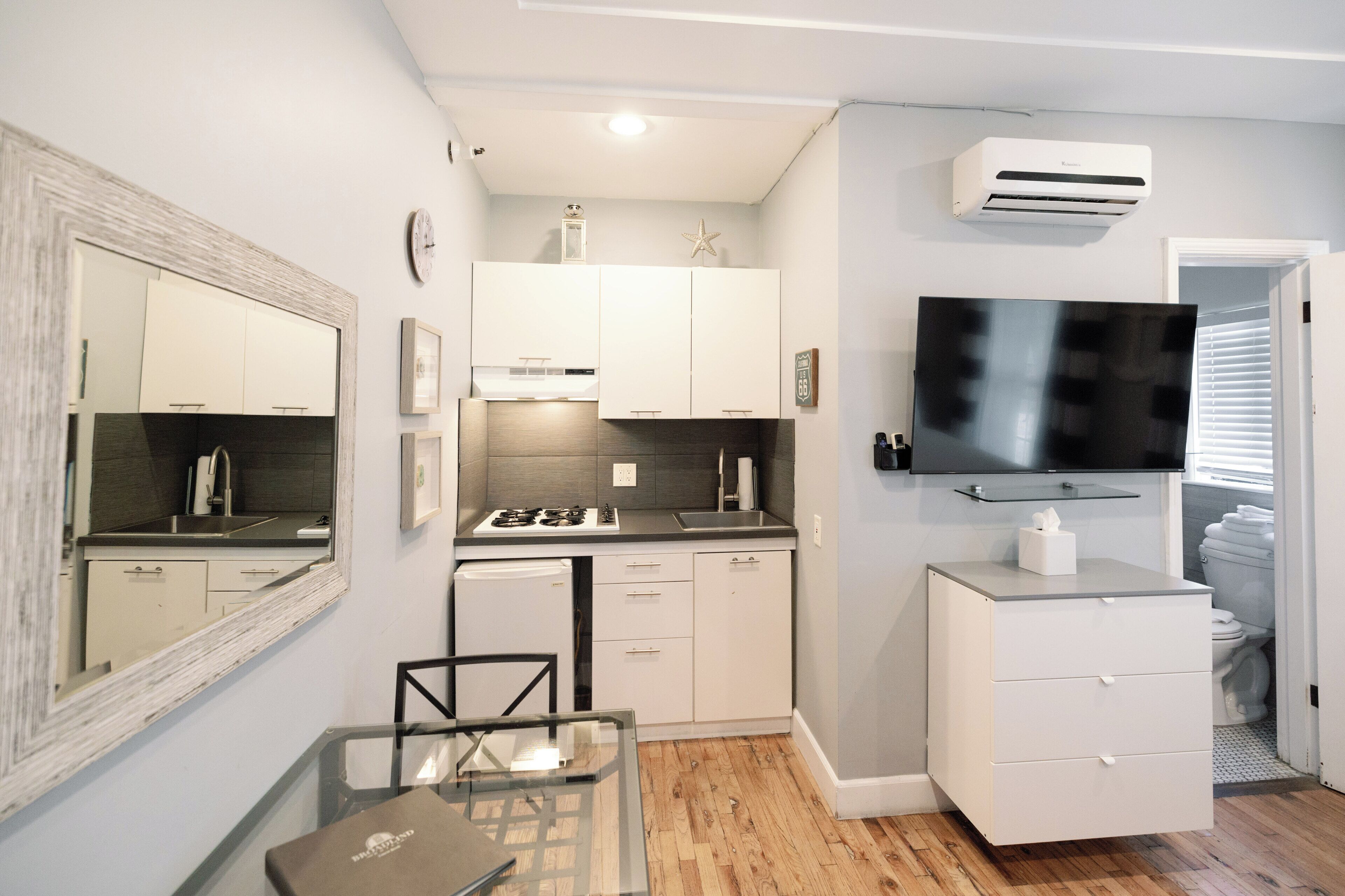 A compact kitchen with white cabinets, a built-in stove, and a flat-screen TV mounted above the counter.