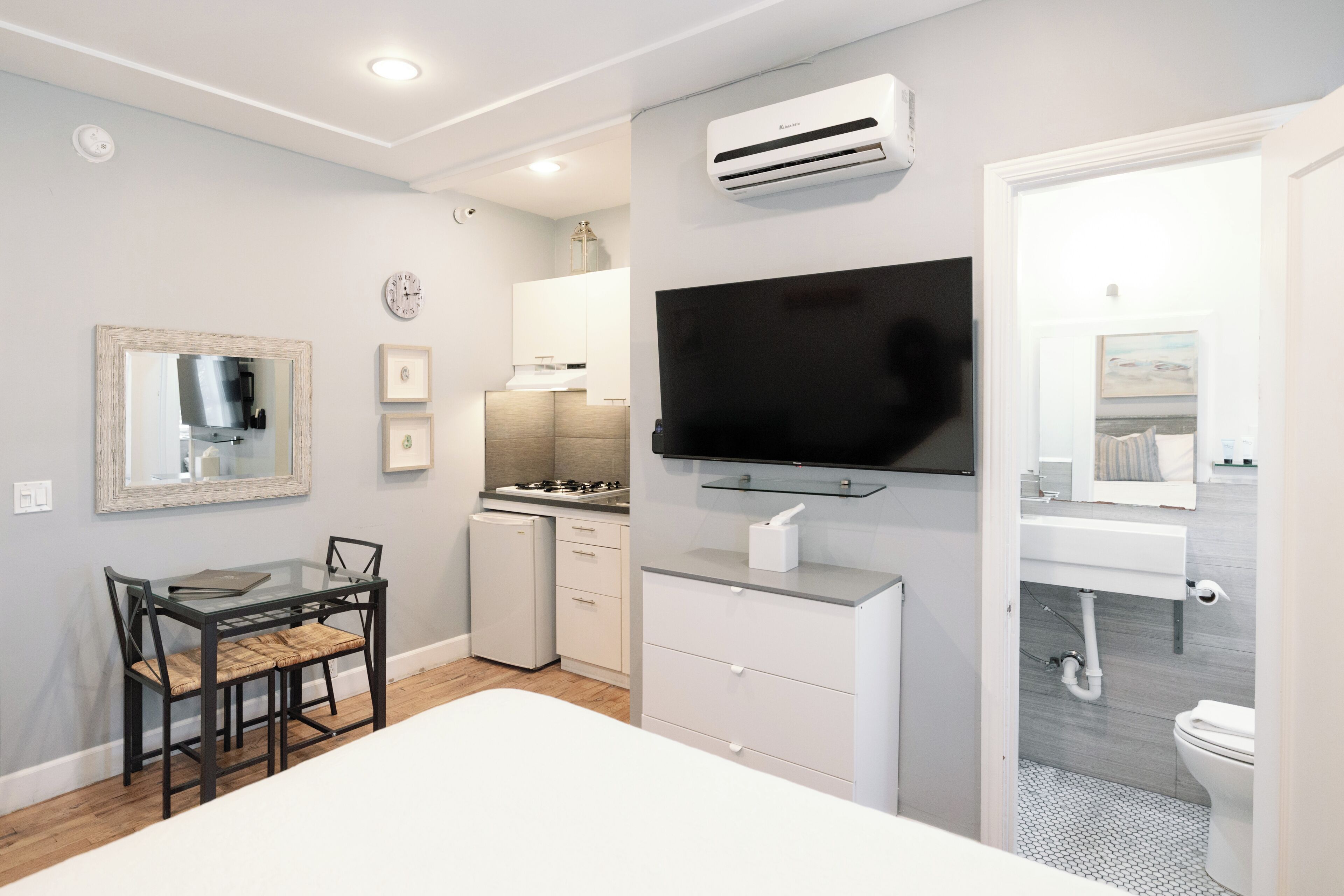A modern hotel room with a bed, a TV, a small kitchenette, and a bathroom.