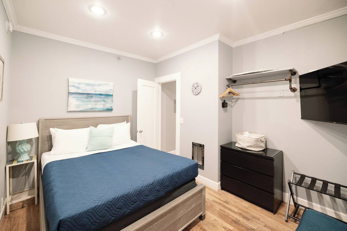 Une chambre à coucher comprenant un lit, une table de chevet, une commode et un téléviseur fixé au mur.